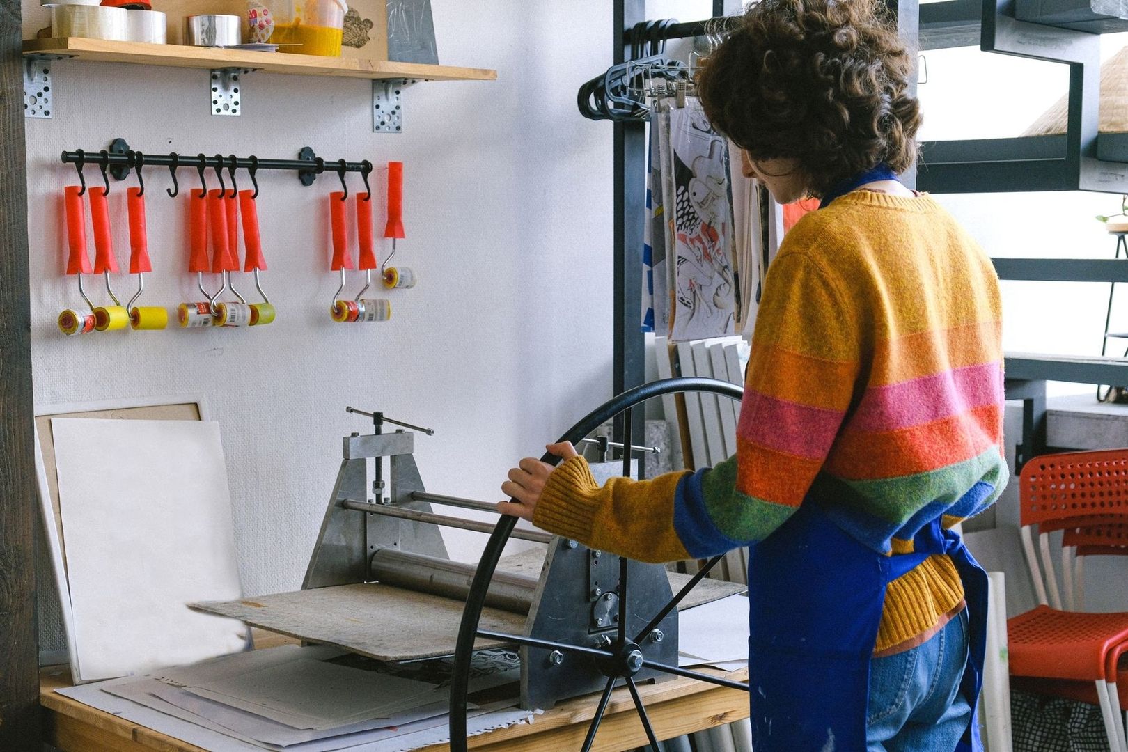 Artist operating a printing press beside hanging rollers in a studio