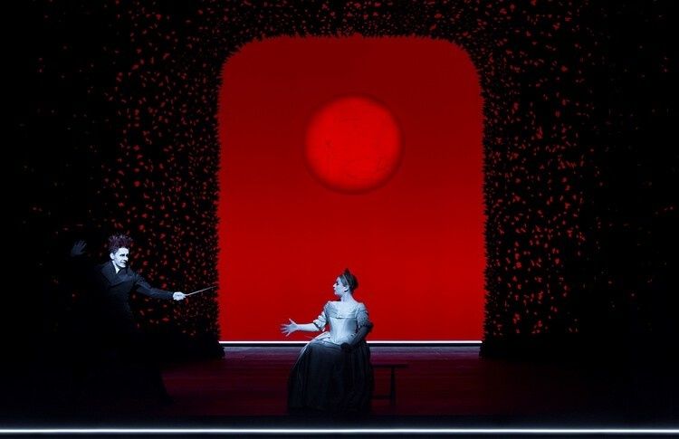 Two actors perform against a stark red backdrop on a dark stage