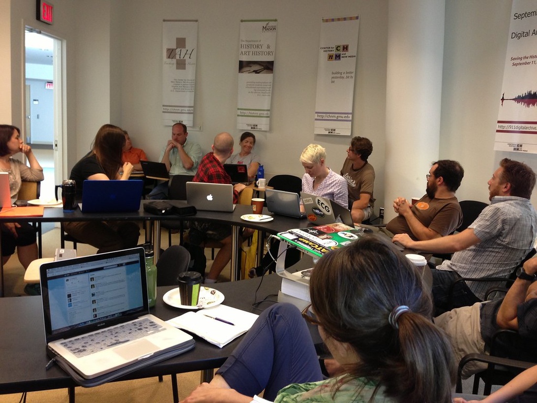 A workshop or classroom setting with multiple people using laptops for learning. Educational banners on the wall display art history content, and participants are engaged in what appears to be a digital learning session or conference.